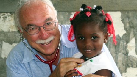Dr. Rolf Maibach hält ein Mädchen auf dem Arm und hört es mit dem Stethoskop ab