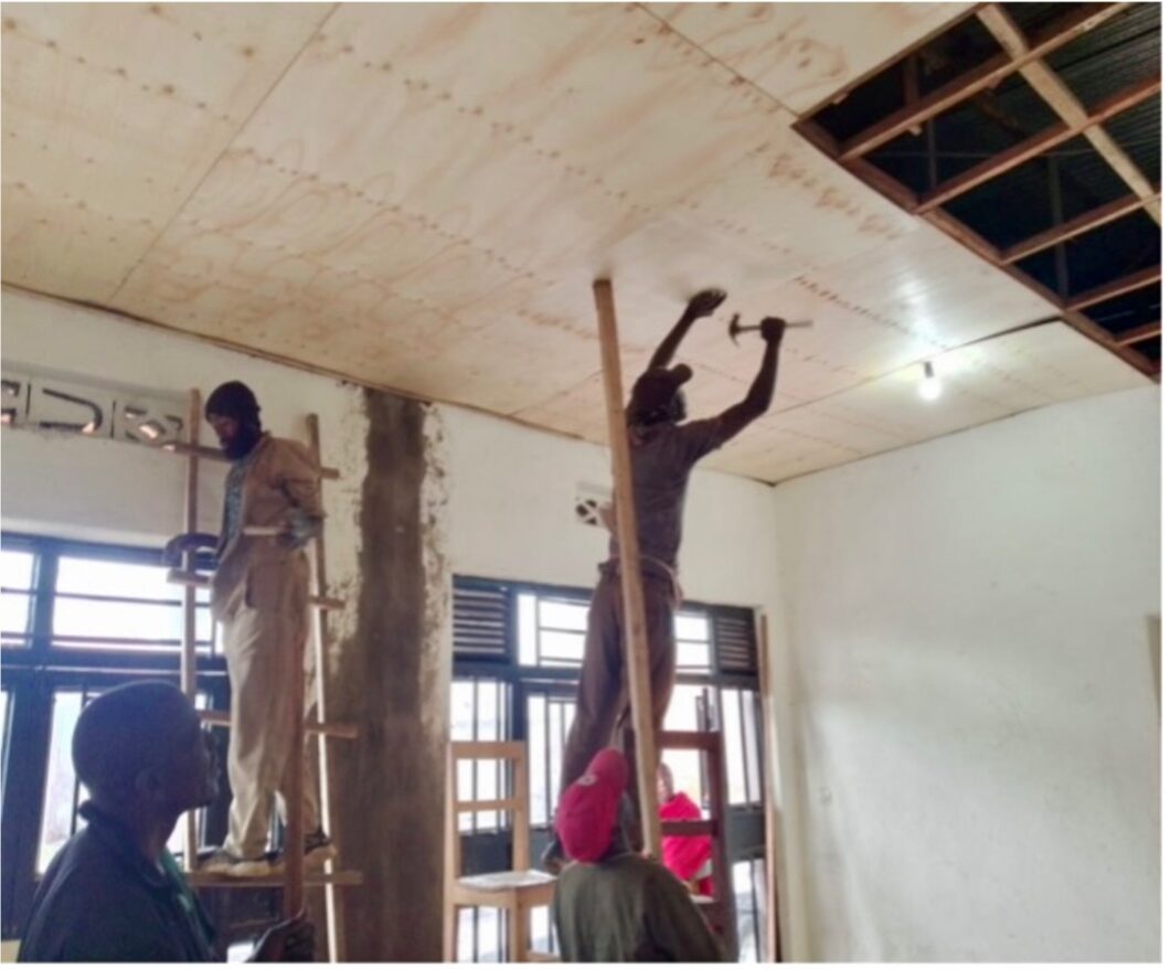 another helper stands on a ladder and nails panels to the ceiling with a hammer to clad it